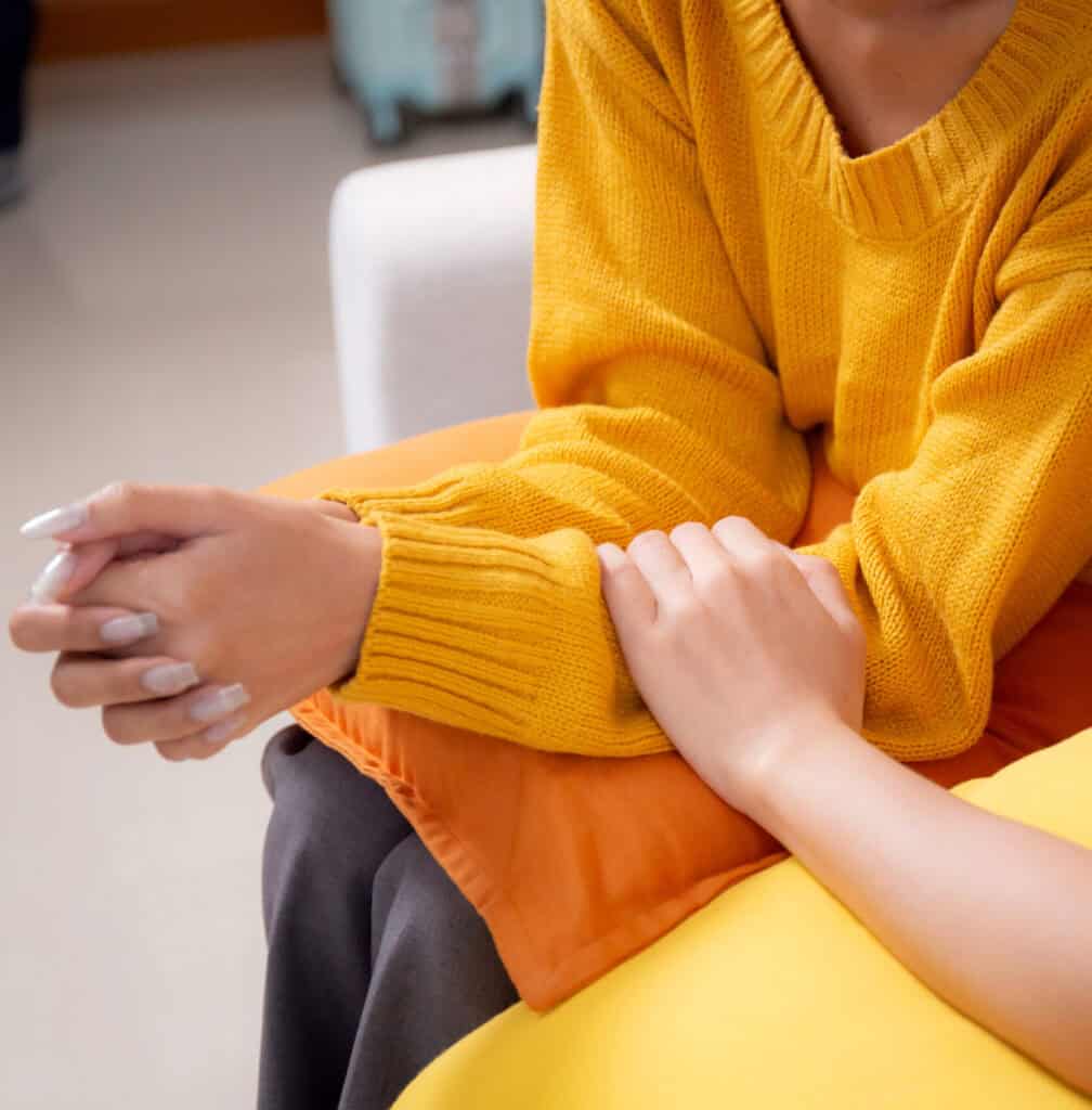 Closeup hand young woman comforting friend with crying and depression sitting on sofa in living room, distress and empathy with friendship, hopelessness and mental health while woman encourage friend.
